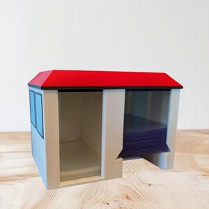 Könnte beinhalten: Ein weiß-roter Kartenhalter mit rotem Dach und schwarzem Rand. Der Kartenhalter hat zwei Abschnitte, einen mit blauen Fenstern und einen mit einem Stapel blauer Karten. Der Halter ist aus Kunststoff.