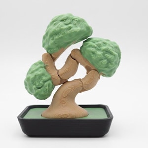 May include: A miniature bonsai tree sculpture with a light green foliage and a light brown trunk. The tree is set in a black rectangular pot with a green interior. The sculpture is a decorative item.