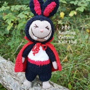Könnte beinhalten: Eine gestrickte Puppe als Vampir verkleidet mit schwarz-roten Hasenohren, einem roten Umhang und einem schwarz-weißen Outfit. Die Puppe hat ein beiges Gesicht mit gestickten Augen, einer kleinen Nase und zwei weißen Fangzähnen. Der Text lautet PDF Knitting Pattern Knit Flat.