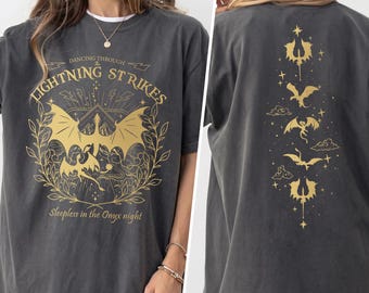 May include: A charcoal gray short-sleeve t-shirt featuring gold graphic prints. The front displays a dragon, foliage, and the text "DANCING THROUGH LIGHTNING STRIKES" and "Sleepless in the Onyx night". The back shows a vertical arrangement of dragons.