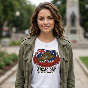 May include: White t-shirt featuring a graphic for Anzac Day. The design includes the Australian flag, a military hat, and red poppies, with the text "ANZAC DAY LEST WE FORGET". The shirt is worn by a person wearing a green jacket.