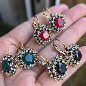 May include: Four pairs of gold-tone dangle earrings with a round, faceted stone centre. The stones are red, green, and black.