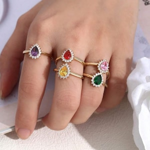 May include: Five gold rings with teardrop-shaped stones. The stones are purple, red, yellow, pink, and green.