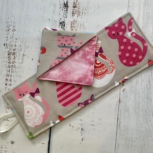 May include: A gray fabric cat-themed coaster and matching folded napkin set. The coaster and napkin feature pink cat illustrations with bows and polka dots. The napkin has a pink tie-dye pattern on the inside and a gray cat print on the outside.