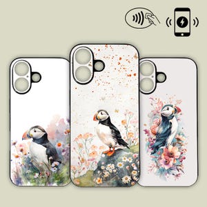 May include: Three phone cases with puffin bird designs. The cases feature watercolor illustrations of puffins with colorful flowers and foliage. The cases are white with black edges and have cutouts for the camera and buttons.