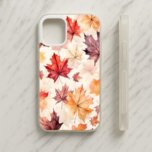 Può includere: Una cover per telefono trasparente con un motivo ad acquerello di foglie d'acero autunnali nei toni del rosso, arancione, giallo e viola scuro su sfondo crema. La cover presenta un ritaglio quadrato per la fotocamera e una vista laterale.
