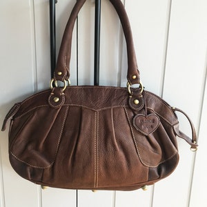 May include: A brown leather handbag with gold hardware and a heart-shaped tag that says "Blondie Mania".