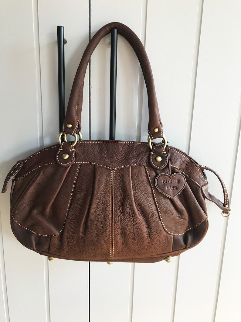 May include: A brown leather handbag with gold hardware and a heart-shaped tag that says "Blondie Mania".