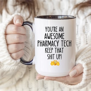 Könnte beinhalten: Weißer Keramikbecher mit schwarzem Innenraum und Henkel. Der Becher trägt den Text "YOU'RE AN AWESOME PHARMACY TECH KEEP THAT SHIT UP!" in Schwarz sowie ein Emoji mit hochgestrecktem Daumen. Der Becher wird von einer Person gehalten.