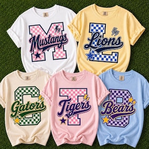 以下が含まれることがあります： 白、黄色、クリーム色、ピンク、水色の半袖Tシャツ5枚。各シャツには、チェック柄の大きなバーシティスタイルの文字、筆記体のチーム名、稲妻や星などのグラフィックアクセントがデザインされています。