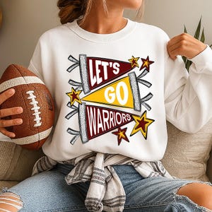 Peut inclure: Sweat-shirt blanc avec un graphisme &laquo; Let's Go Warriors &raquo; dans des motifs de fanions marron, jaune et blanc, avec des &eacute;toiles. Un ballon de football marron est tenu dans la main gauche.
