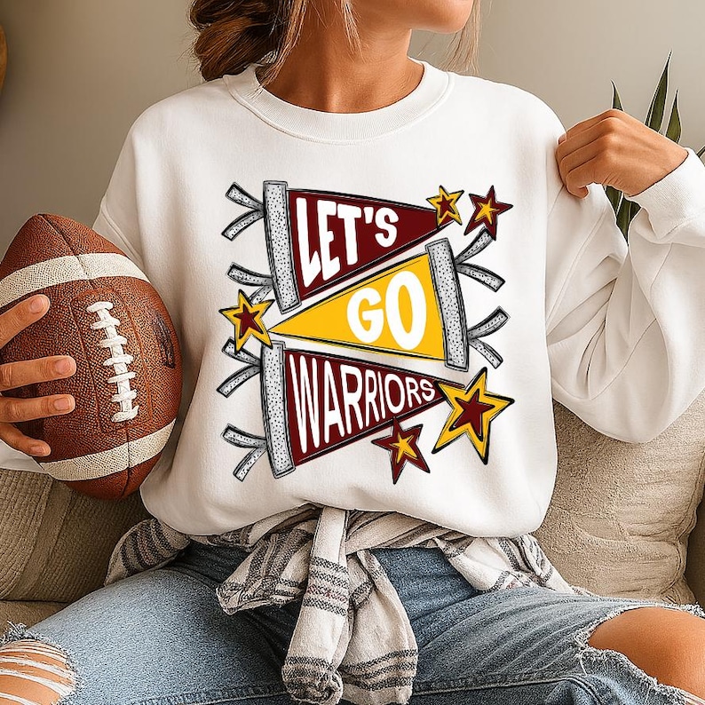 Peut inclure: Sweat-shirt blanc avec un graphisme &laquo; Let's Go Warriors &raquo; dans des motifs de fanions marron, jaune et blanc, avec des &eacute;toiles. Un ballon de football marron est tenu dans la main gauche.