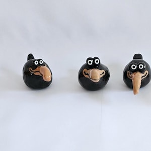 Könnte beinhalten: Vier schwarze Keramik-Vogelfiguren mit großen Augen und langen, braunen Schnäbeln. Die Vögel sind in einer Reihe auf weißem Hintergrund angeordnet.