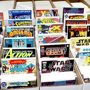 May include: A collection of comic books displayed in cardboard boxes. Titles include "Superman," "X-Men," "Star Wars," and "Thor." The covers feature vibrant colors and various superhero illustrations, showcasing a variety of comic book series.