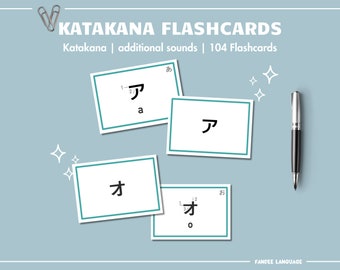 May include: Katakana flashcards with Japanese characters and English transliterations. The flashcards are white with a teal border and are arranged on a light blue background. A silver and black pen and a paperclip are also present.