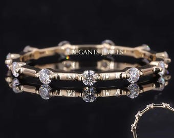 May include: A gold-colored ring with multiple clear, round gemstones set around the band. The ring is displayed on a reflective black surface, showcasing its design and sparkle. The ring is a piece of jewelry.