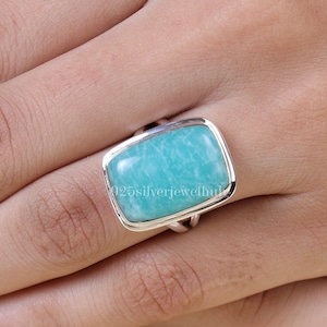 Könnte beinhalten: Ein silberner Ring mit einem rechteckigen, hellblauen Edelstein. Der Ring hat ein schlichtes, elegantes Design.