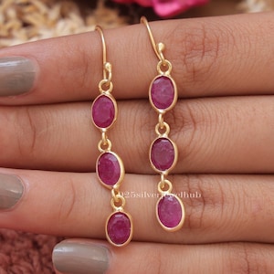 Pode incluir: Brincos de ouro com quatro pedras de rubi ovais penduradas em um gancho de ouro.