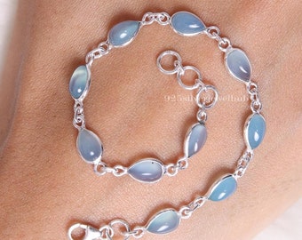 Könnte beinhalten: Ein silbernes Kettenarmband mit mehreren glatten, tropfenförmigen hellblauen Steinen in Metallfassungen. Das Armband verfügt über einen Karabinerverschluss und eine verstellbare Verlängerungskette mit runden Gliedern. Der Text 925silverjewelhub ist sichtbar.
