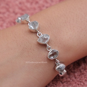 Puede incluir: Una pulsera de cadena de plata con cinco piedras irregulares, transparentes y de corte bruto engastadas en biseles de plata pulida. Las piedras están unidas en fila y el texto 925silverjewelhub aparece en pequeñas letras blancas.