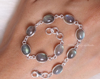 May include: A silver chain bracelet featuring eight oval-shaped, iridescent labradorite gemstones set in polished metal bezels. The bracelet includes a lobster claw clasp and a short extender chain. The text 925silverjewelhub is visible.