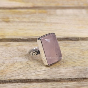 Pode incluir: Um anel de prata com uma pedra retangular de quartzo rosa. A banda do anel tem um design decorativo.