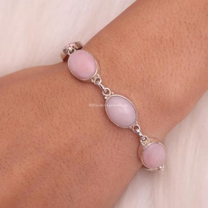 Peut inclure: Un bracelet à chaîne en argent composé de trois pierres ovales rose clair lisses serties dans des chatons en argent poli. Le bracelet est relié par de petits maillons en argent et affiche le texte 925silverjewelhub au centre de l'image.