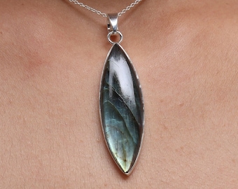 May include: A marquise-shaped labradorite gemstone pendant set in a polished silver bezel. The stone displays iridescent blue and gray flashes across its smooth surface. The pendant hangs from a delicate silver chain, resting against the skin.