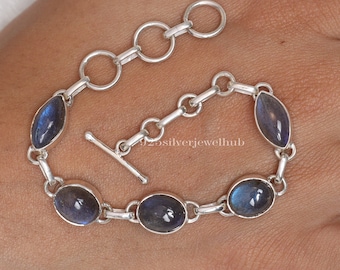 May include: A silver bracelet featuring five oval-shaped labradorite gemstones with blue iridescence, connected by silver links. The bracelet includes a toggle clasp and an adjustable chain with circular links. The text 925silverjewelhub is visible.