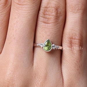 May include: A silver ring with a pear-shaped green gemstone. The ring has small silver accents on either side of the stone.