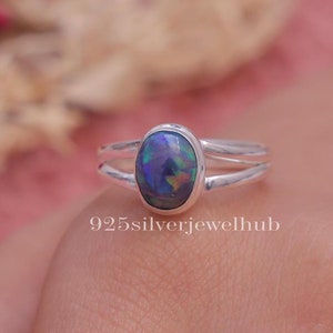 May include: A sterling silver ring featuring an oval-shaped dark opal gemstone with iridescent flashes of blue, green, and orange. The band is split into two thin, polished silver strands. The text 925silverjewelhub is printed below the ring.