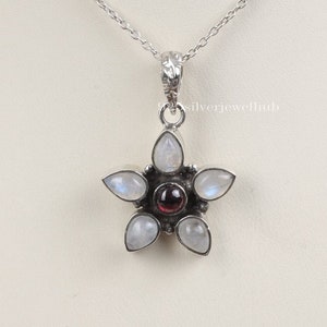 May include: A silver pendant necklace with a star-shaped design. The star is made of six moonstone stones and a red garnet in the center.