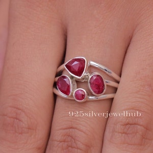 May include: A silver ring featuring four faceted red stones of varying shapes and sizes, including a triangular, a pear, an oval, and a small round stone, all set in a multi-band silver frame with the text 925silverjewelhub visible on the image.