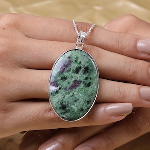 Puede incluir: Un collar de cadena de plata con un colgante ovalado con una piedra preciosa de zoisita verde y rosa.