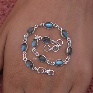 May include: A silver chain bracelet featuring eight oval-shaped labradorite gemstones with blue and grey iridescence. The bracelet includes a lobster claw clasp and an adjustable extender chain. The text 925silverjewelhub is visible in the center.