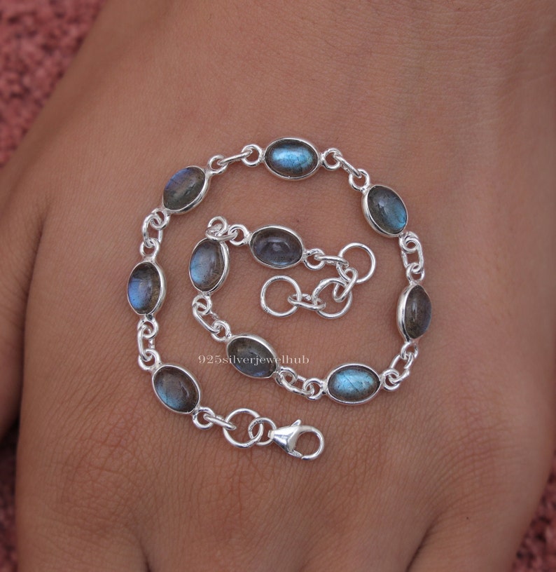 May include: A silver chain bracelet featuring eight oval-shaped labradorite gemstones with blue and grey iridescence. The bracelet includes a lobster claw clasp and an adjustable extender chain. The text 925silverjewelhub is visible in the center.