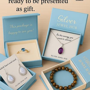 May include: Four light blue jewelry boxes containing a gold ring with a blue stone, a silver necklace with a purple pendant, silver teardrop earrings with iridescent stones, and a brown beaded bracelet, with text printed on the boxes and cards.