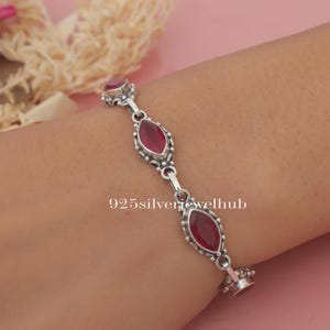 May include: A silver bracelet with four red gemstone accents. The bracelet has a delicate chain design and is adorned with intricate details.