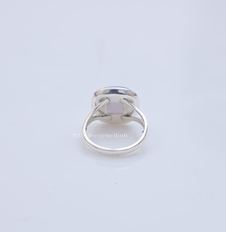 May include: A silver ring featuring a square-shaped, light purple gemstone set in a polished metal band. The setting includes four prongs holding the stone, with a split shank design. The text 925ilverjewelhub is visible on the band.
