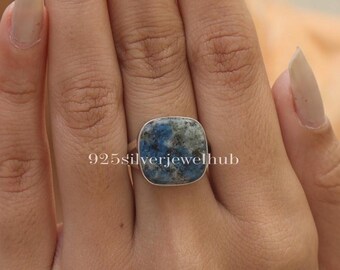 Puede incluir: Un anillo de plata con una piedra preciosa cuadrada azul y blanca. El anillo está en el dedo de una persona.