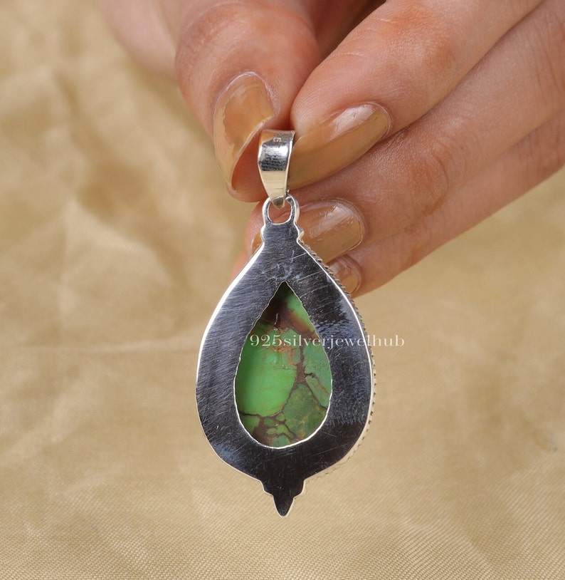 May include: A silver pendant with a green turquoise stone set in a teardrop shape. The pendant has a bail at the top for attaching to a chain.