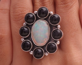 May include: A silver ring with a large white opal gemstone surrounded by eight smaller black onyx gemstones.