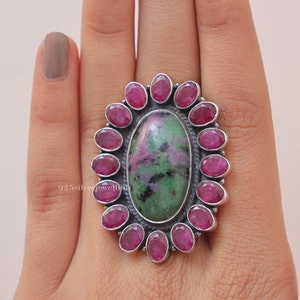 Könnte beinhalten: Ein silberner Ring mit einem großen ovalen grün-rosa Edelstein, umgeben von einem Heiligenschein aus kleineren rosa Edelsteinen.