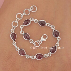 May include: A silver bracelet featuring teardrop-shaped, deep red gemstones. The bracelet is linked with small, circular silver connectors and has a lobster clasp. The text "925silverjewelhub" is visible on the bracelet.