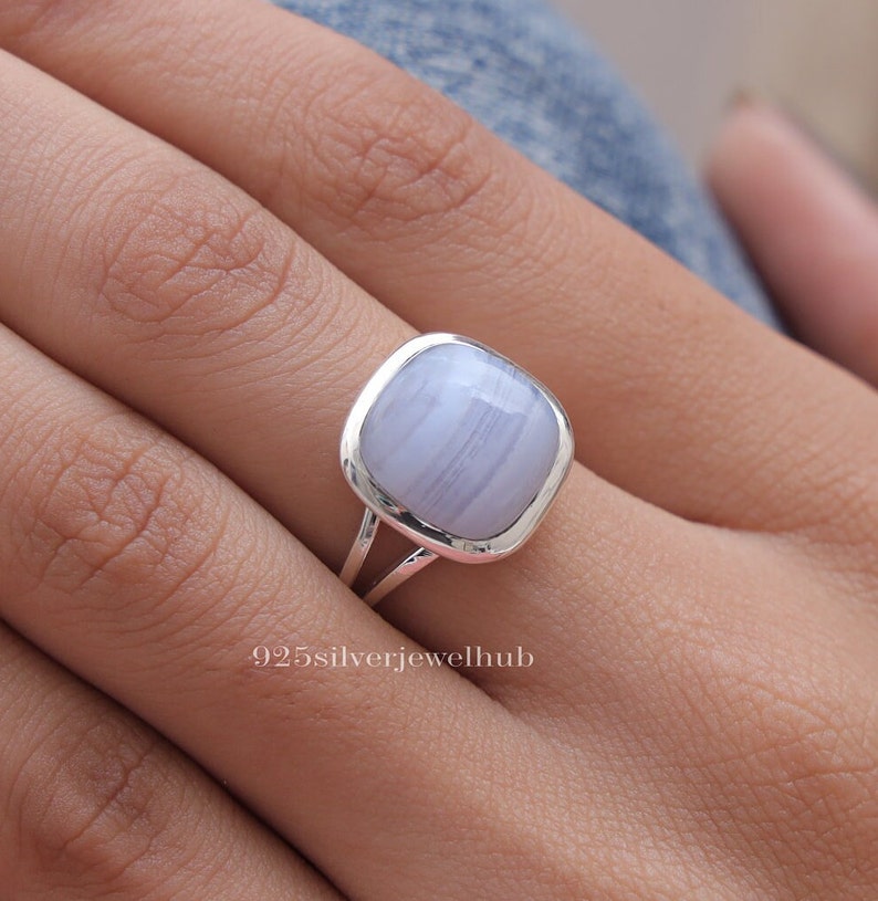 May include: A silver ring featuring a smooth, square-shaped light blue chalcedony gemstone with subtle white banding. The stone is set in a polished silver bezel on a split-shank band. The text 925silverjewelhub is visible at the bottom.