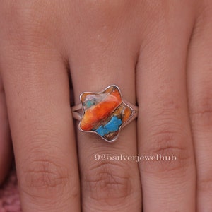 May include: A star-shaped ring with a silver band. The ring features a colorful stone with orange, turquoise, and white hues. The text "925silverjewelhub" is visible at the bottom of the image.