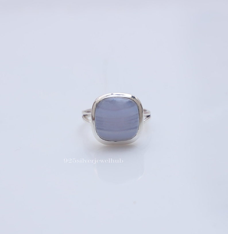 May include: A silver ring featuring a smooth, cushion-cut, light blue chalcedony gemstone with subtle horizontal banding. The metal band has a split design on the sides. The text 925silverjewelhub is printed in white below the ring.