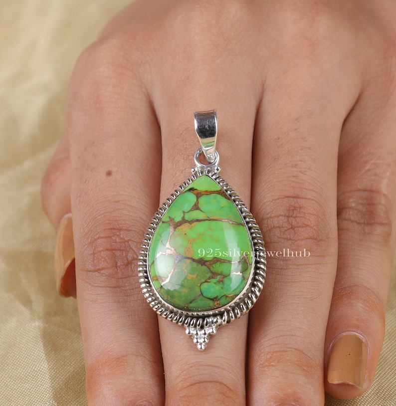 May include: A teardrop-shaped pendant with a green turquoise stone set in sterling silver. The pendant has a detailed silver border and a small silver bail.