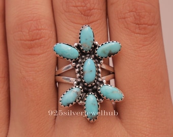 Puede incluir: Un anillo de plata de ley con siete piedras de turquesa de forma ovalada dispuestas en un racimo floral. La piedra central está rodeada por seis piedras radiantes, todas engastadas en biseles dentados. El texto 925silverjewelhub es visible.