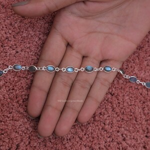 May include: A silver chain bracelet featuring a series of oval-shaped labradorite gemstones. Each stone is set in a simple silver bezel and connected by small silver circular links. The bracelet includes a lobster claw clasp and a small extender chain.
